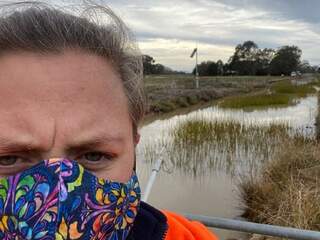 Photograph of GMW employee Dannielle Ick in high vis and a face mask in front of a channel lined with weeds