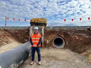 Photograph of Phillip Sibio standing in front of a drainage works project in high vis and a hard hat with a large metre wide pipe in view
