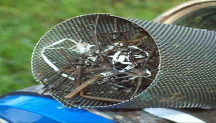 An image of a strainer on a pipe blocked with grass and debris